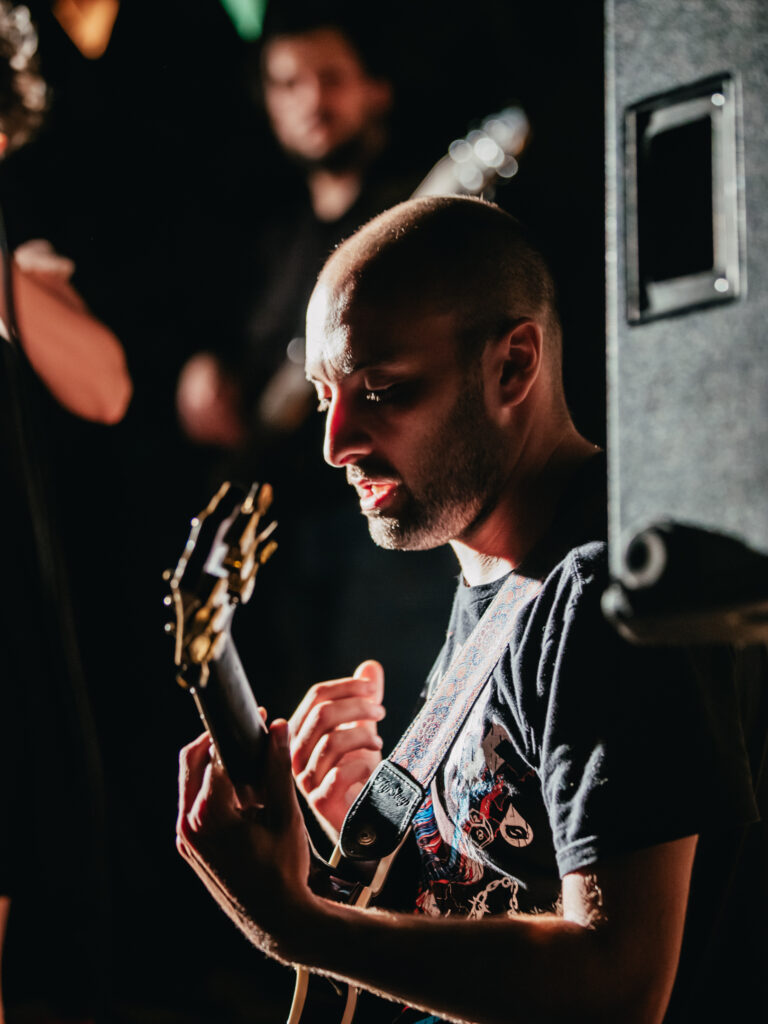 Estudiante de Nivel Superior de Collegium tocando la guitarra con la cabeza inclinada, durante una guitarreada estudiantil
